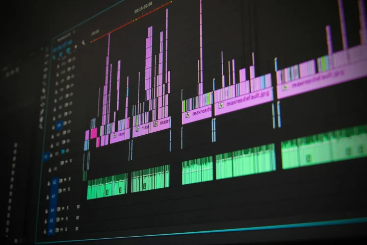 Computer screen shows audio waveforms in pink, purple, and green on dark tracks.