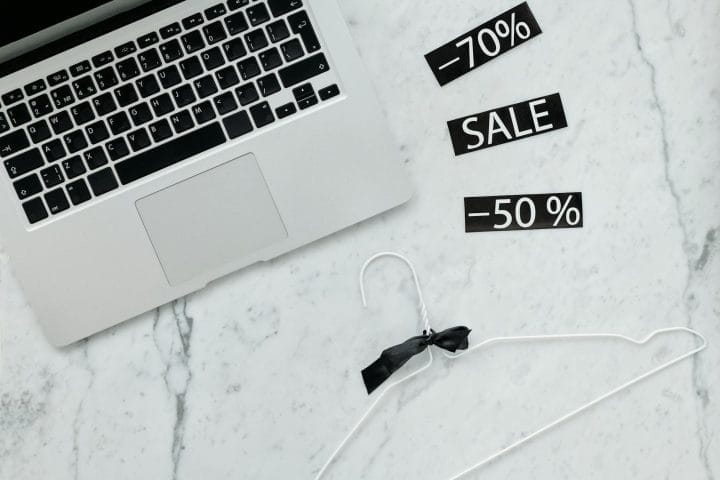 Silver laptop on marble table with 70% off and 50% off sale tags nearby.