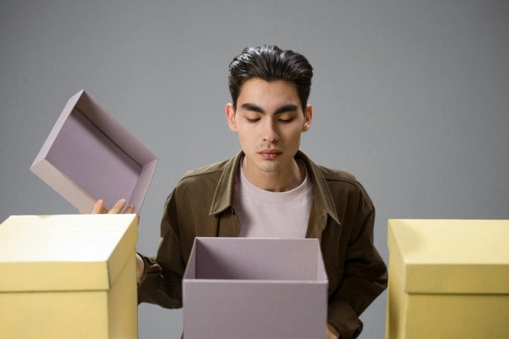 A young man peers inside an open purple box with yellow boxes nearby.