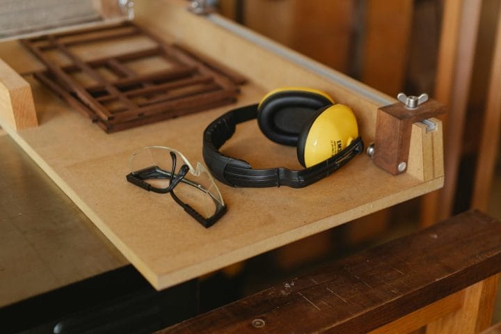 Clear goggles and black-yellow earmuffs on a workshop table with clamps.
