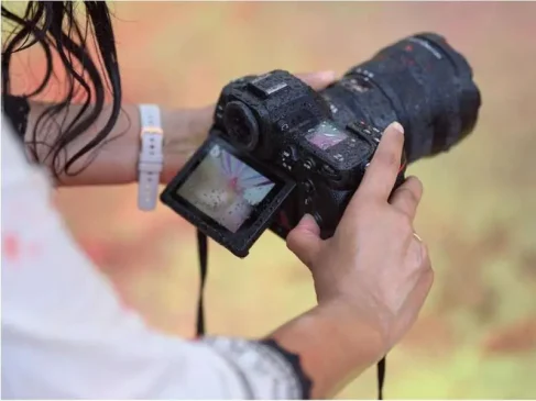Woman's hands grip a wet Nikon mirrorless camera; flipped LCD screen shows a photo with water droplets.