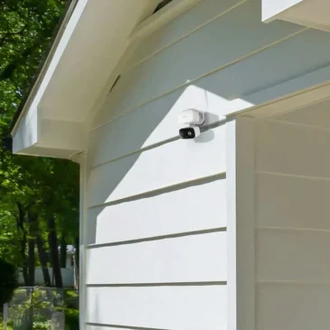 White dome security camera mounted high on a garage wall under the eaves.