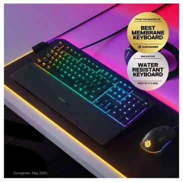 SteelSeries gaming keyboard with RGB lights sits on a glowing pad next to a matching mouse and shows Eurogamer awards for best membrane keyboard.