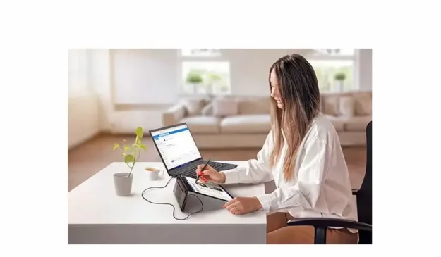 Woman using a Lenovo ThinkVision portable touch monitor with a laptop on a desk.