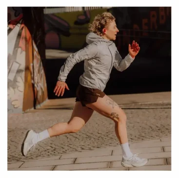 Woman running outdoors in a gray jacket and white shoes.